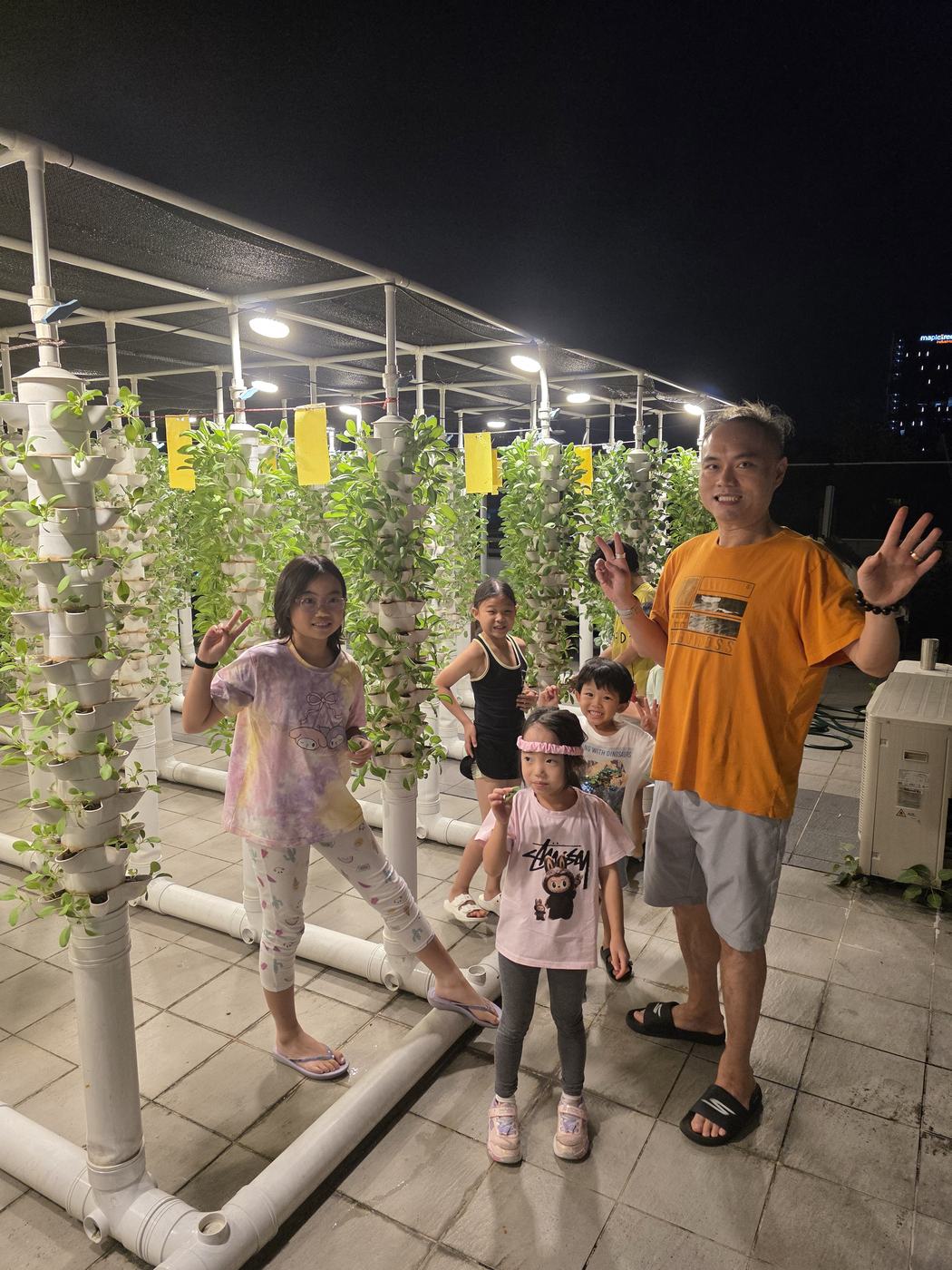 Children and an adult standing together among the white vertical grow towers at the Two Doctors Aquaponics farm in Kallang