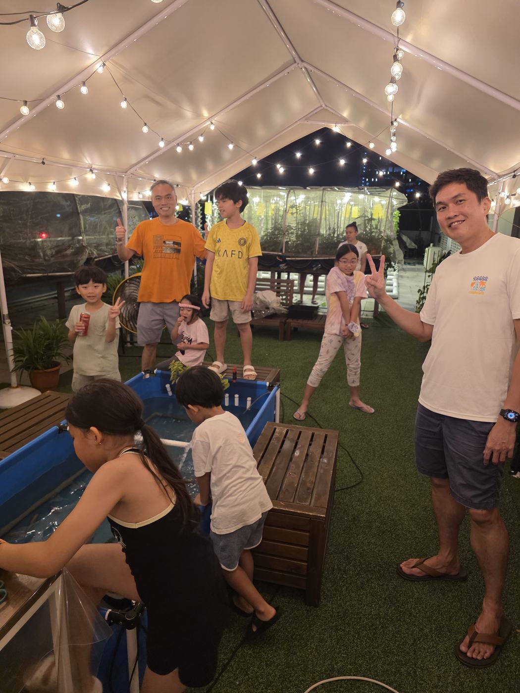 Children feeding fish at an aquaponics tank during an evening farm visit in Singapore